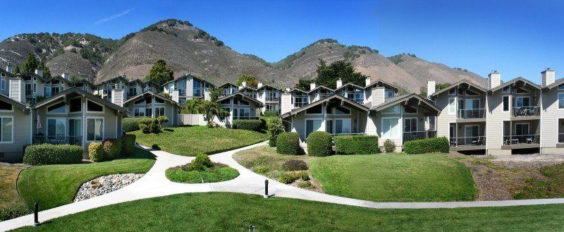 Exterior view of tan townhomes with green grass, hills in background
